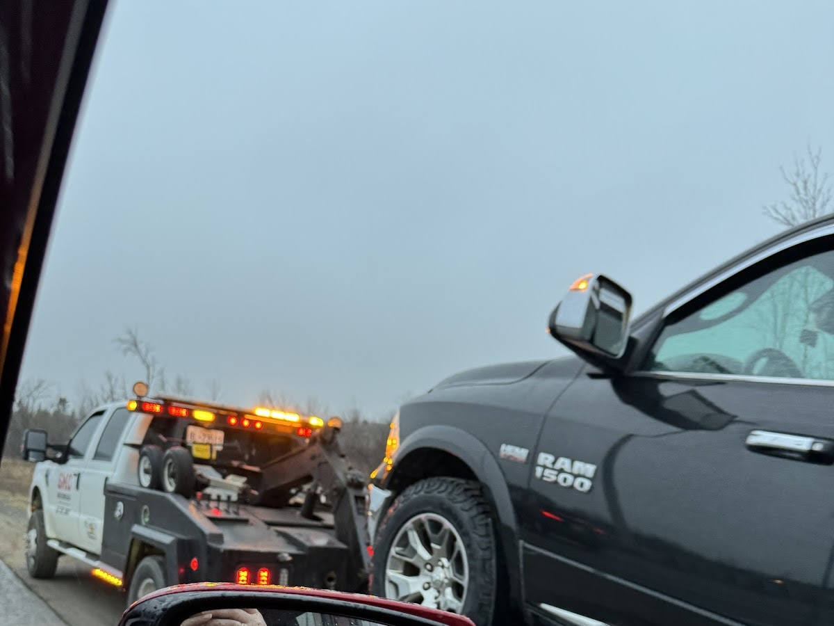 Roadside assistance truck with emergency lights stopped beside a pickup truck on an overcast day